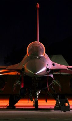 a fighter jet sitting on top of an airport tarmac at night with its lights on