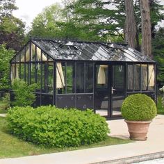 a small black greenhouse in the middle of a garden with trees and bushes around it