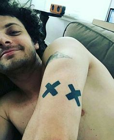 a shirtless man laying on top of a couch next to a pillow with crosses tattooed on his arm