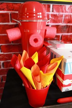 a red fire hydrant sitting on top of a table next to a bunch of paper flowers