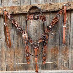 a brown horse bridle and reins hanging on a wooden wall next to a fence