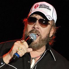 a man with sunglasses and a hat on holding a microphone in his right hand while singing into a mic