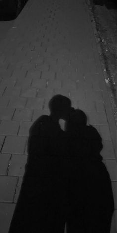 the shadow of two people standing next to each other in front of a brick sidewalk