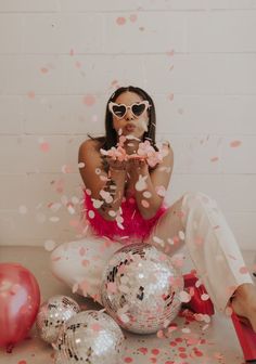 a woman sitting on the floor surrounded by confetti and balloons with her hands in her mouth