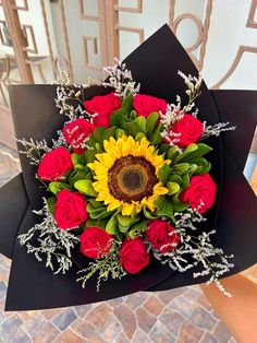 a bouquet of roses and sunflowers on top of a black paper with greenery