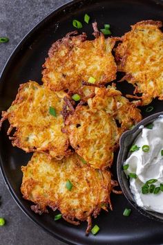 some fried food on a black plate with sour cream and green onions next to it