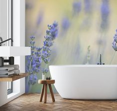 a bath tub sitting next to a wall with lavender flowers on the side and a wooden stool