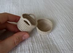 a hand holding two crocheted baby shoes on top of a white bed sheet