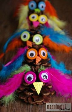 three fake birds made out of pine cones with googly eyes and feathers on them