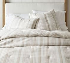 an unmade bed with white and beige striped sheets