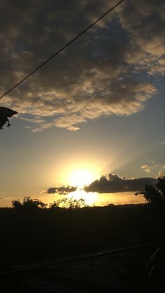 the sun is setting behind some clouds in the sky with power lines running through it