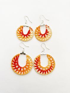 three pairs of orange and white crocheted hoop earrings with silver hooks on a white background