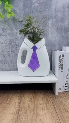 a white vase with a purple tie on it sitting next to a book and plant