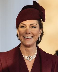 a woman in a red suit and hat smiles at the camera while wearing pearls on her necklace