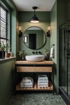 a bathroom with green walls and a round mirror above the sink, surrounded by towels