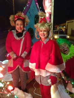 two women dressed up in costumes standing next to each other near christmas decorations and lights