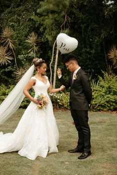 a bride and groom standing in the grass holding balloons with their names written on them