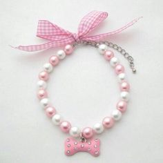 a bracelet with pink and white pearls and a bow charm on it, sitting on top of