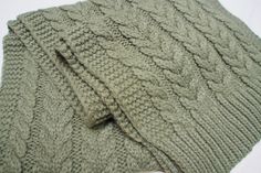 a green knitted sweater laying on top of a white surface