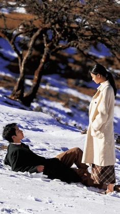 a man laying in the snow next to a woman