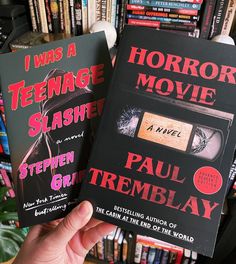 two books in front of a book shelf with many books on it and one being held up to the camera