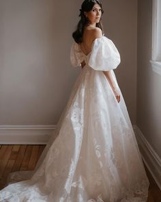 a woman in a white wedding dress is standing by a window and looking off to the side