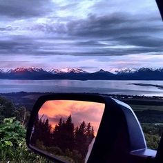 the view from inside a car looking out at mountains and water with clouds in the sky