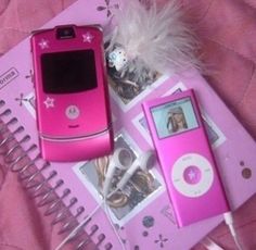 two pink cell phones sitting next to each other on top of a notebook with ear buds