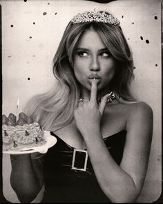 black and white photograph of a woman holding a cake with her finger to her lips