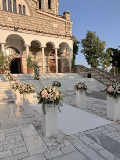 three white vases filled with flowers sitting on top of a stone walkway next to a building