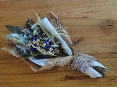 a bouquet of dried flowers is wrapped in brown paper and tied with twine on a wooden table