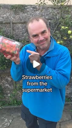 a man in blue jacket holding up a jar filled with fruit and pointing to the camera