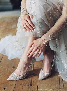 a woman in white dress sitting on the floor with her hand on her wedding shoe