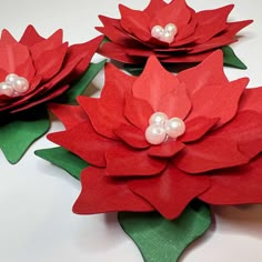 three paper poinsettis with pearls on them sitting on top of each other