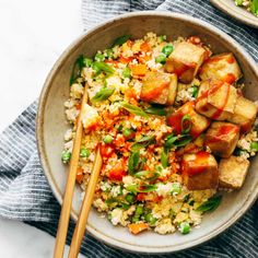 two bowls filled with rice, tofu and veggies next to chopsticks