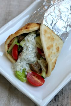 a pita filled with meat and vegetables on top of foil wrapper sitting on a white plate