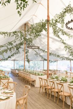 an indoor tent with tables and chairs set up for a formal dinner or party, surrounded by greenery