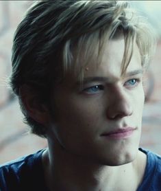 a young man with blue eyes stares into the distance while standing in front of a brick wall