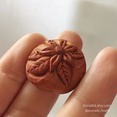 a hand is holding a ring made out of clay with leaves on the front and back