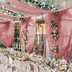 a long table with white chairs and pink drapes