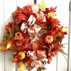 a wreath with fall leaves and pumpkins hanging on a door