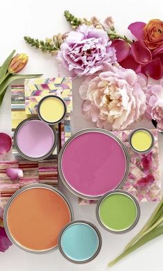 various colors of paint next to flowers on a white surface with pink peonies