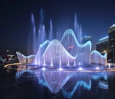 an illuminated fountain in the middle of a city at night