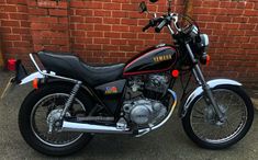 a black and red yamaha motorcycle parked in front of a brick wall