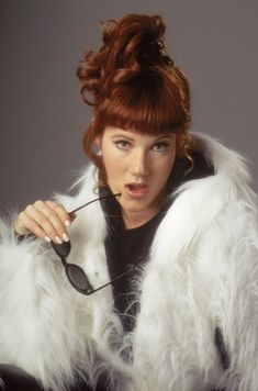 a woman with red hair wearing a white fur coat and holding a pair of sunglasses