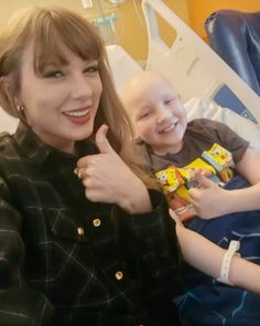 a woman giving the thumbs up while sitting next to a child in a hospital bed