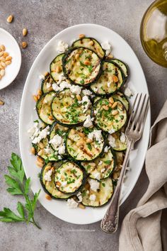 a white plate topped with zucchini slices covered in feta cheese and nuts