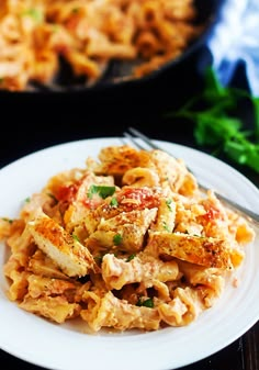 a white plate topped with pasta next to a skillet filled with meat and vegetables