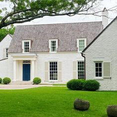 a white brick house with blue door and two large rocks in front of it on the grass