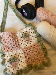 a crocheted purse sitting on top of a bed next to yarn and headphones